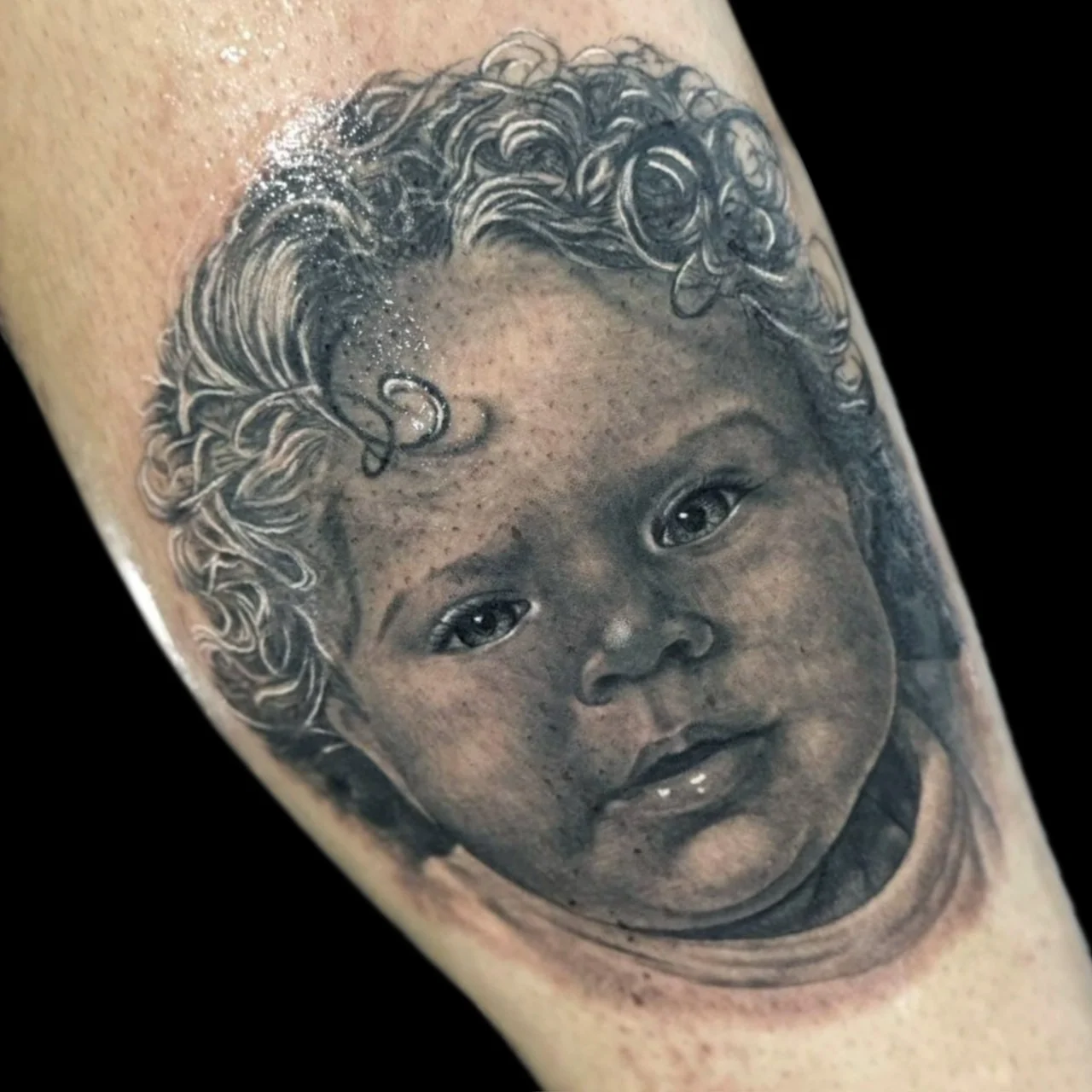 Black and grey realism portrait tattoo of a young child with curly hair and freckles on the arm at Bloodline Tattoo Bangkok.