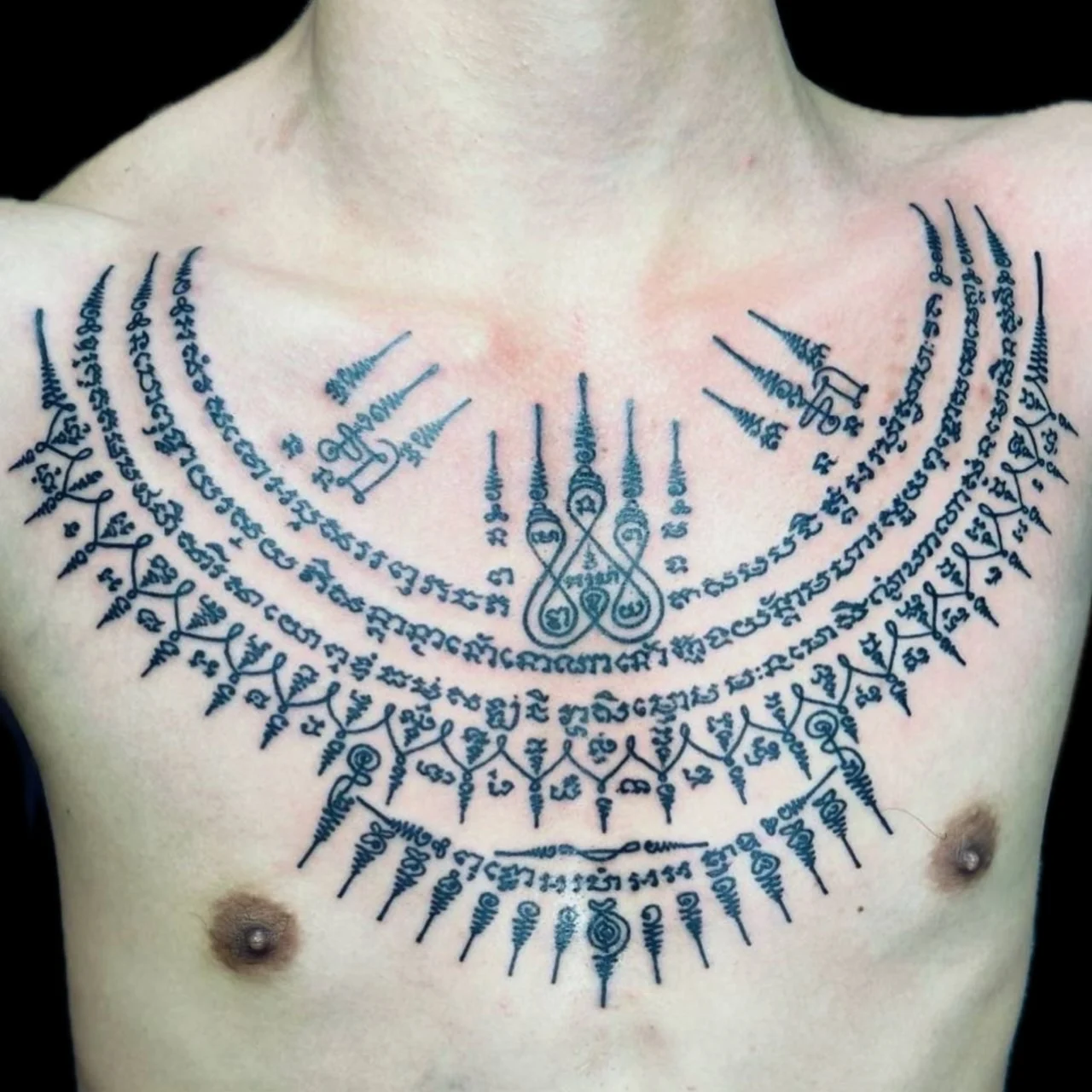 Sak Yant chest collar tattoo with Khom script arcs, central yantra spires, and symmetrical sacred geometry across the upper chest at Bloodline Tattoo Bangkok.