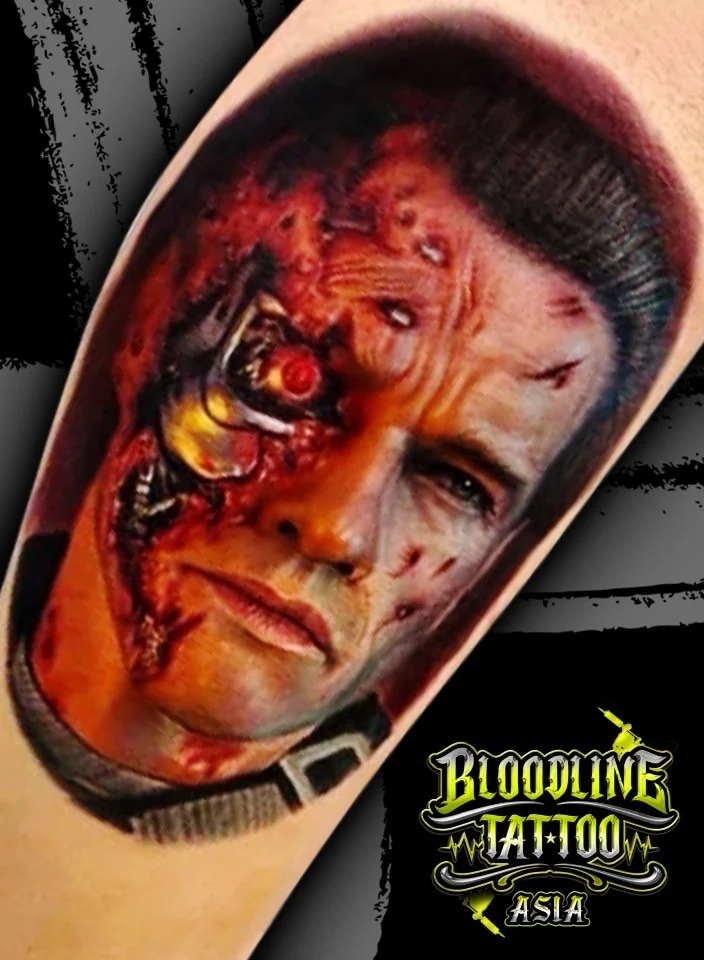 Colour portrait realism tattoo of battle-damaged Terminator with exposed endoskeleton and glowing red eye at Bloodline Tattoo Bangkok.