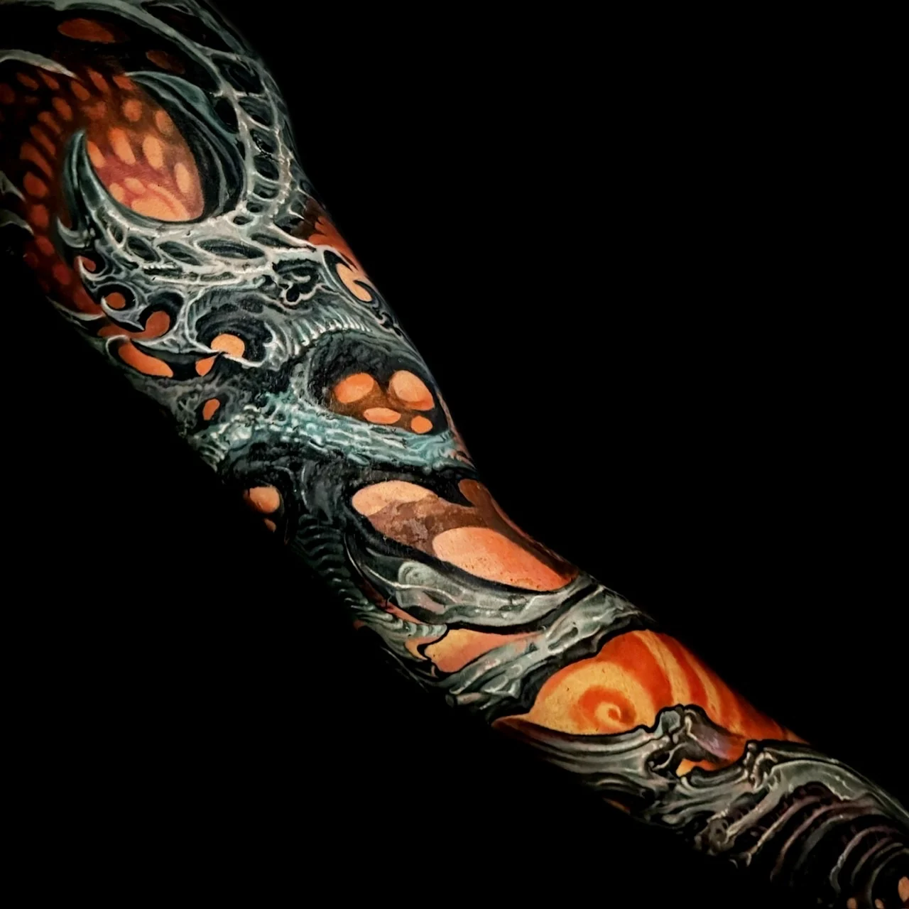 Colour biomechanical full sleeve tattoo with dark metallic structures and glowing orange organic accents on the arm at Bloodline Tattoo Bangkok.