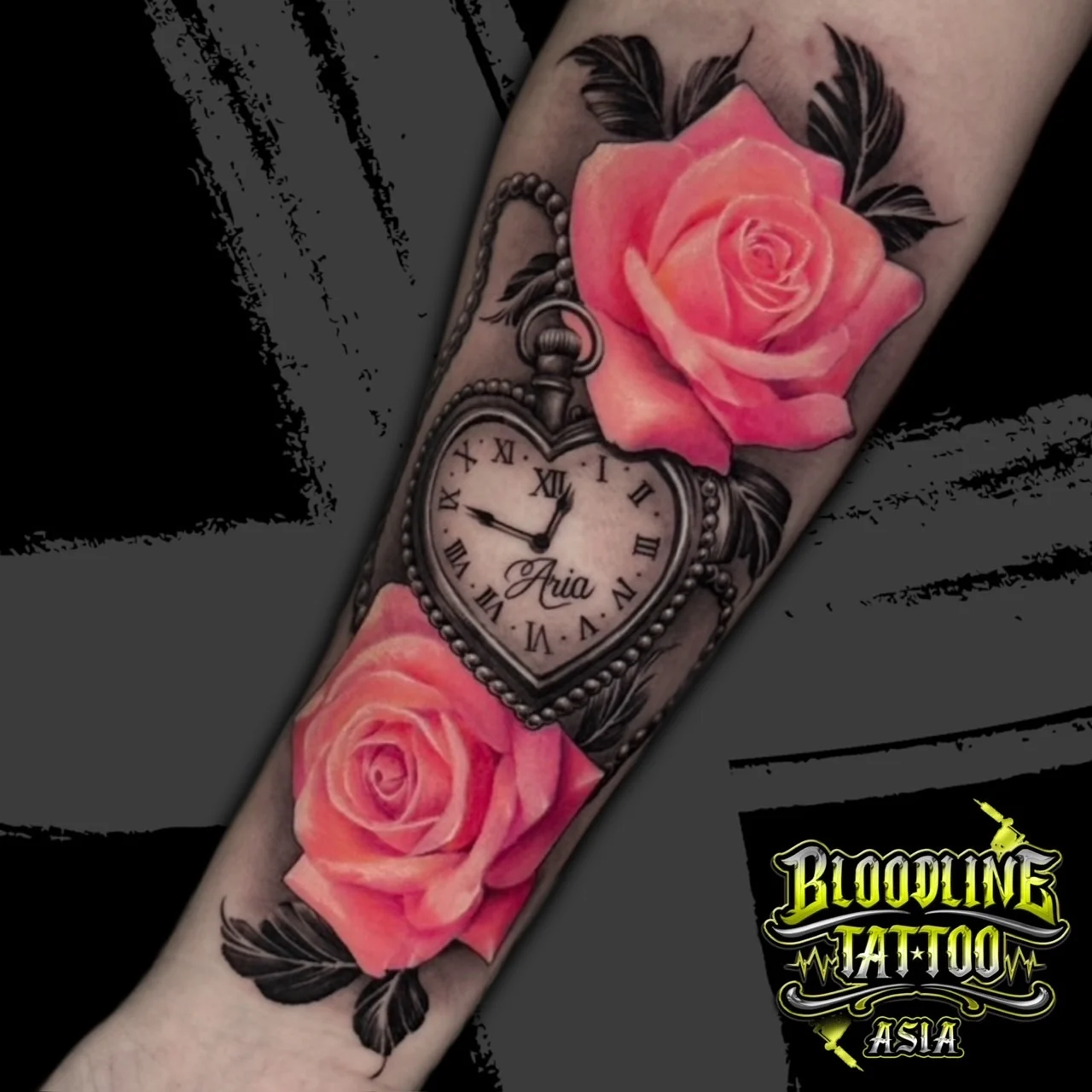 Colour realistic forearm tattoo of a heart-shaped pocket watch inscribed Aria flanked by pink roses at Bloodline Tattoo Bangkok.