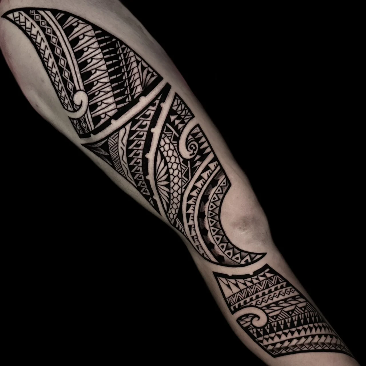 Large leg tattoo with angular blackwork panels of Polynesian-inspired geometric patterns, scales, and fine-line tribal ornament, at Bloodline Tattoo Bangkok.