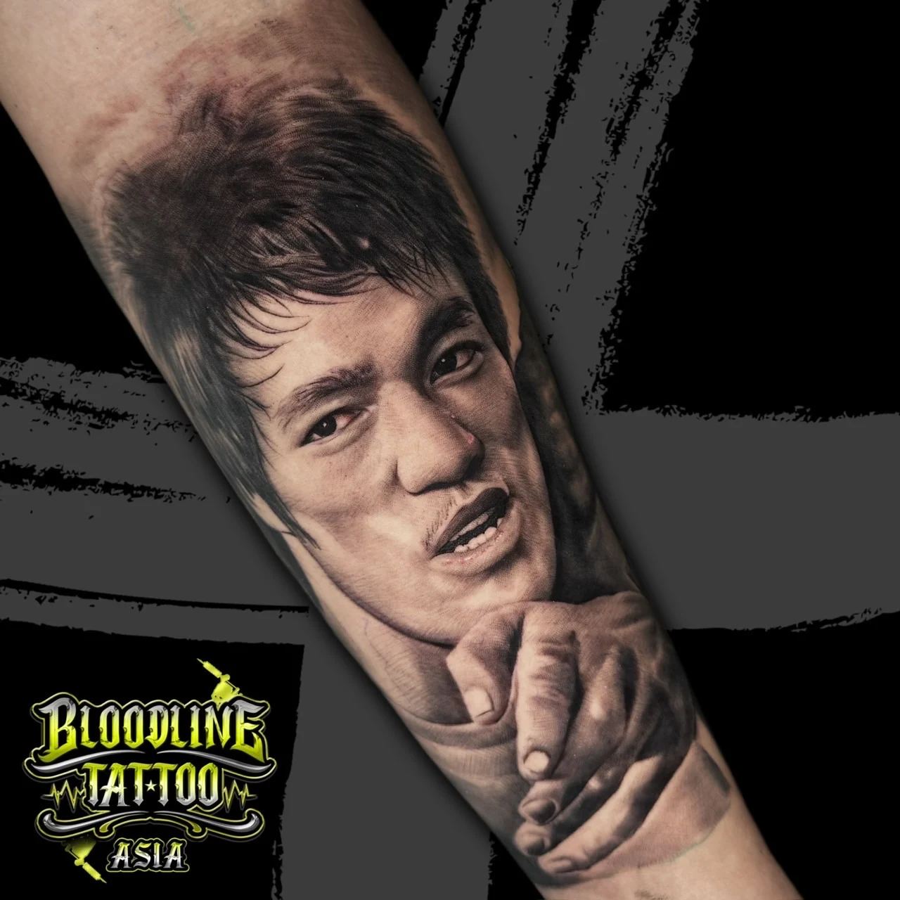 Black and grey portrait realism forearm tattoo of Bruce Lee pointing directly forward with intense facial detail at Bloodline Tattoo Bangkok.