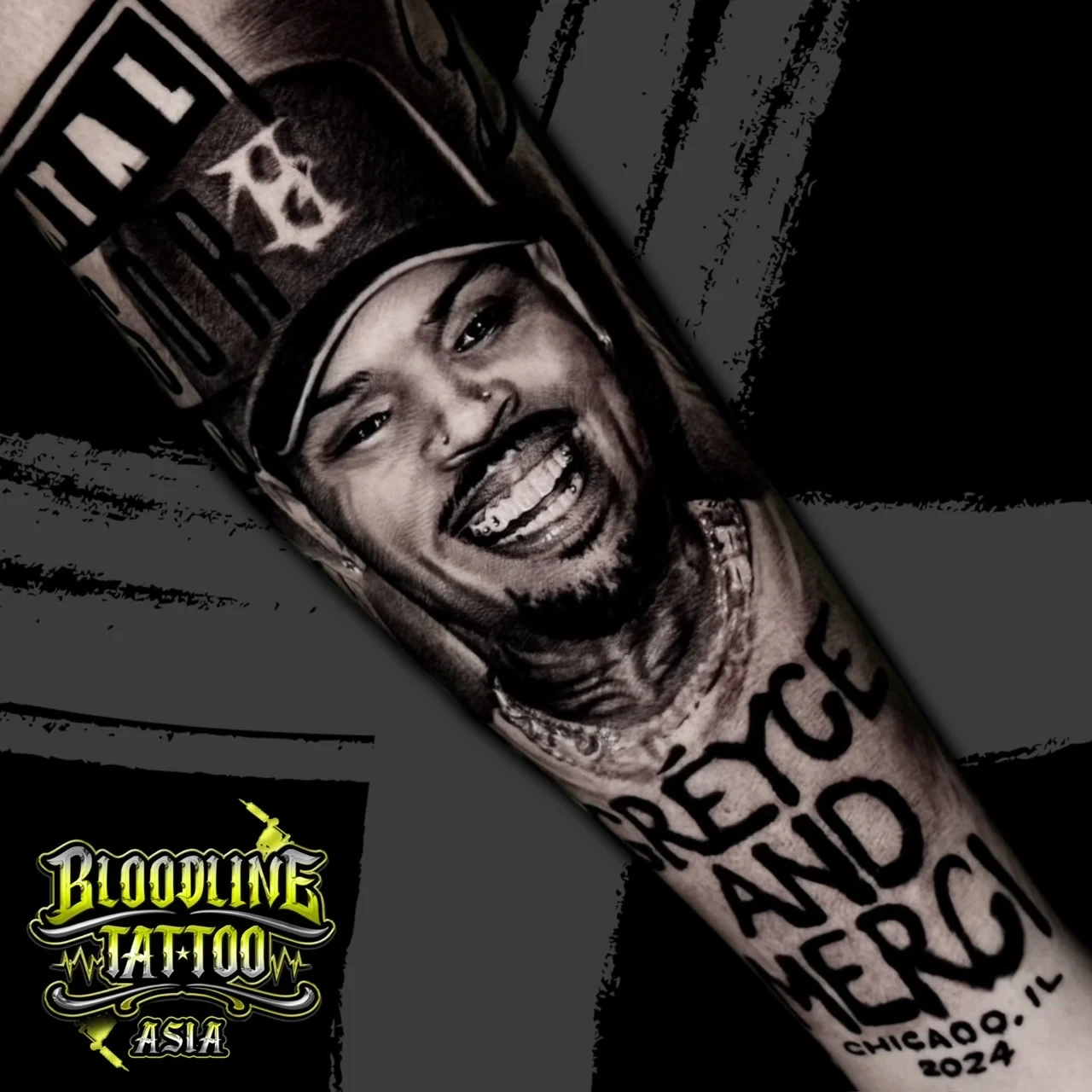 Black and grey portrait realism forearm tattoo of Chris Brown in a cap with grills and bold Greyce and Merci Chicago script below at Bloodline Tattoo Bangkok.