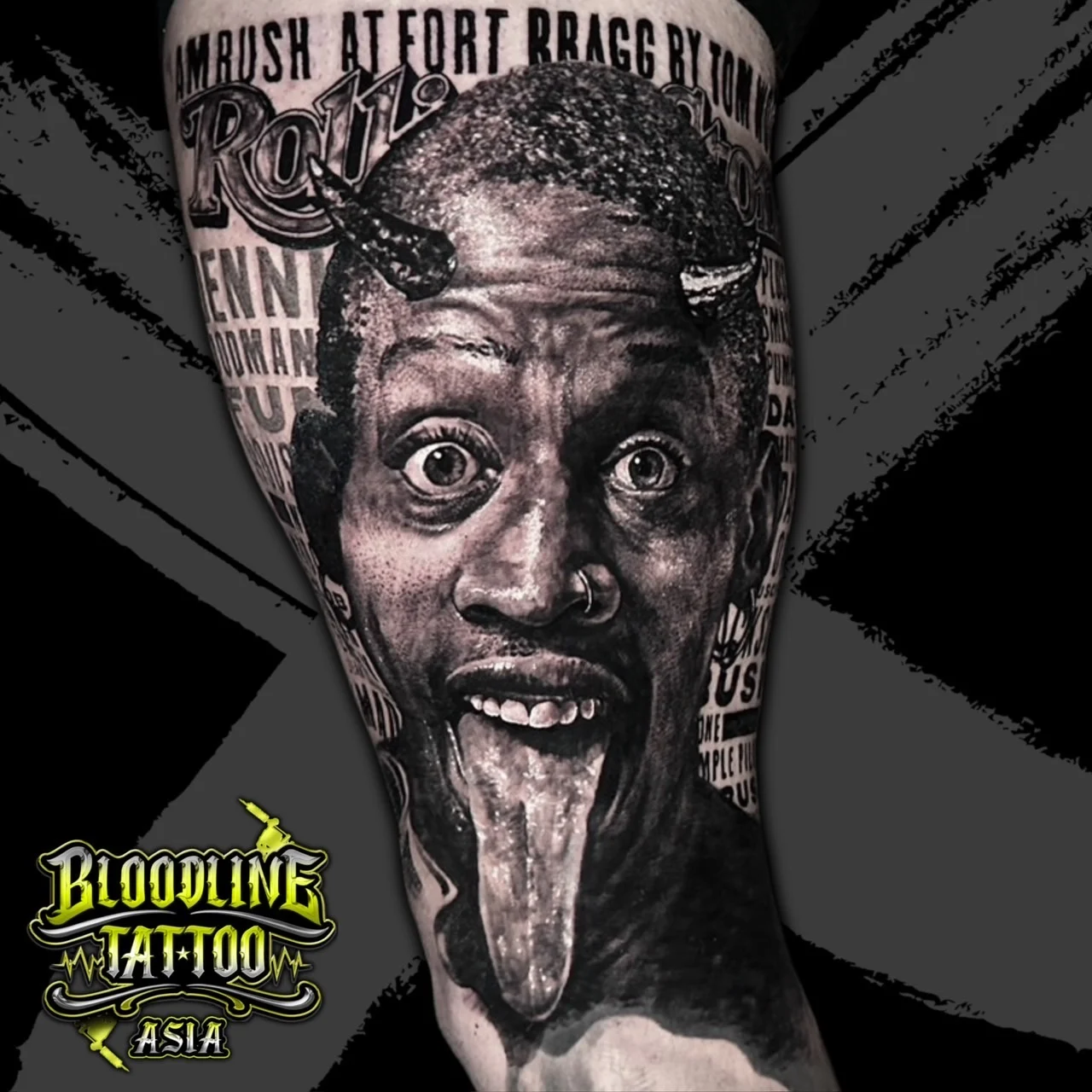 Black and grey portrait realism arm tattoo of Dennis Rodman with devil horns, tongue out, nose ring, and newspaper typography background at Bloodline Tattoo Bangkok.