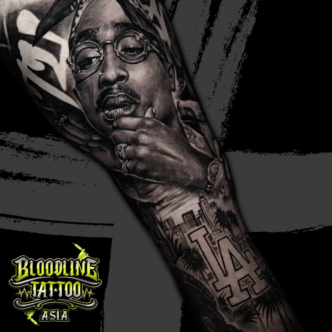 Black and grey portrait realism forearm sleeve of Tupac Shakur in bandana and glasses with Los Angeles skyline, palm trees, and Dodgers LA logo at Bloodline Tattoo Bangkok.
