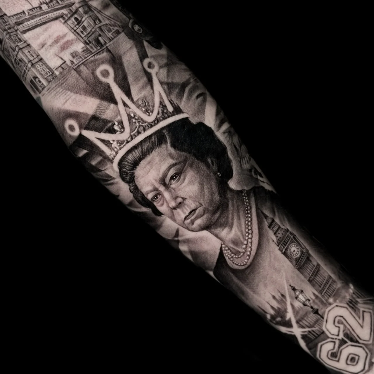 A black and grey realism arm sleeve centered on Queen Elizabeth II with Tower Bridge, Big Ben, and a faded Union Jack backdrop, at Bloodline Tattoo Bangkok.