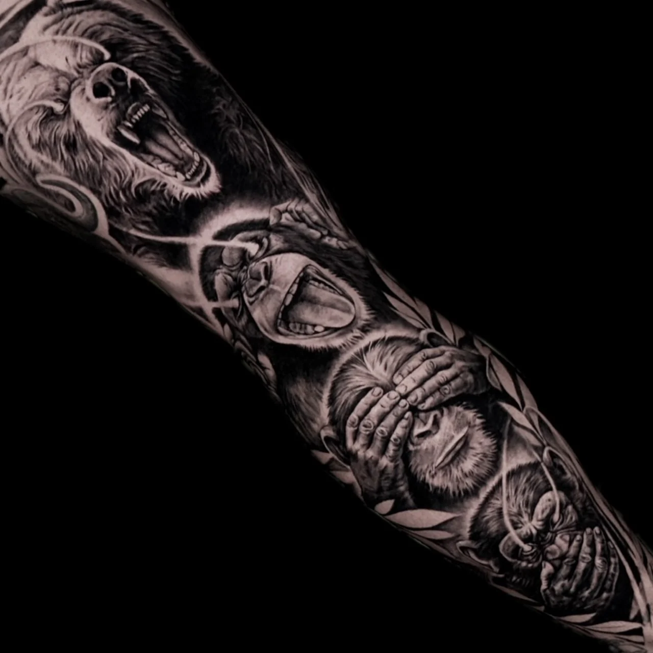 A black and grey realism sleeve with a roaring grizzly bear above the three wise monkeys motif with glowing eye highlights, at Bloodline Tattoo Bangkok.