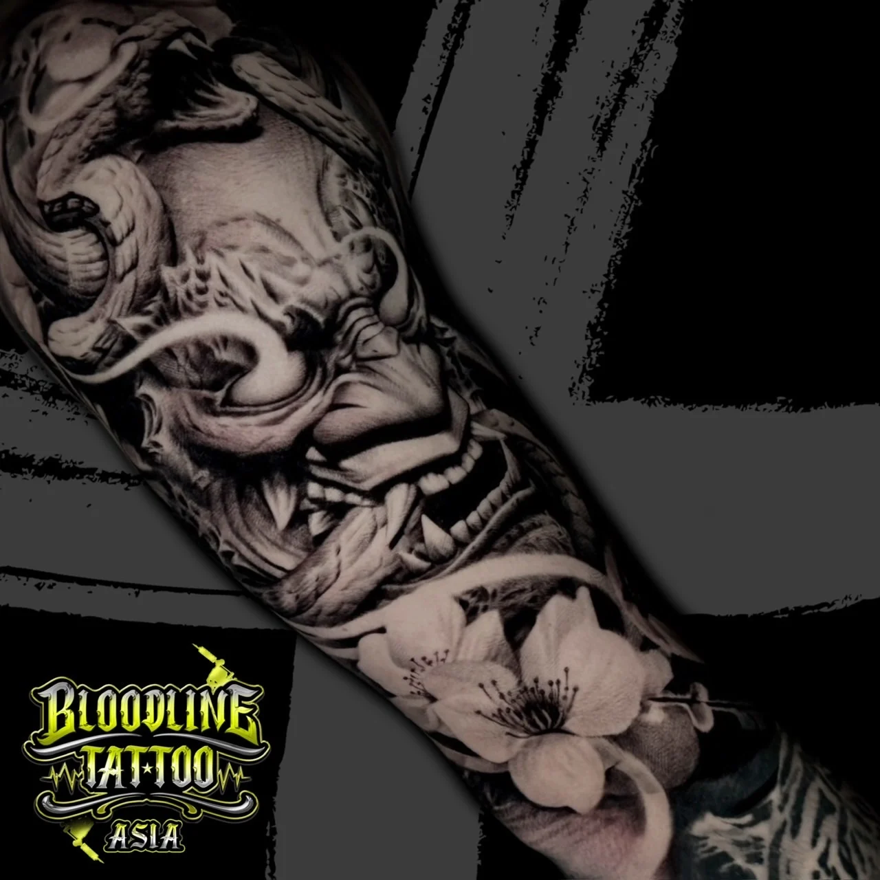 A black and grey realism forearm sleeve of a fierce Hannya mask entwined with a scaled snake and delicate cherry blossoms, at Bloodline Tattoo Bangkok.